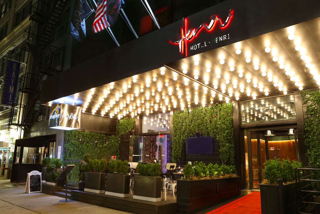 Hotel Henri NYC exterior entrance at night with bright lights, greenery, and welcoming ambiance